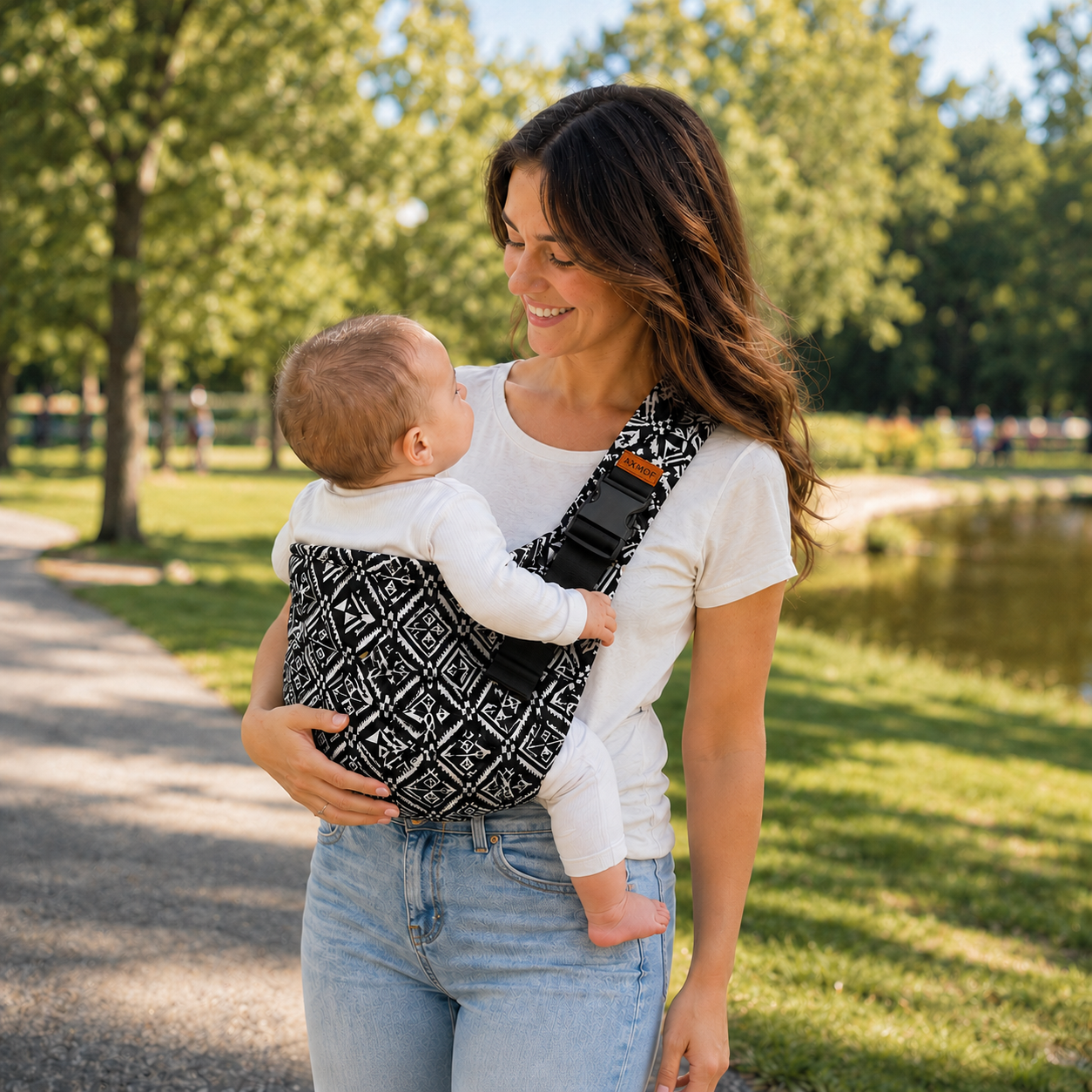 Woman holding a baby in a carrier outdoors near a pond